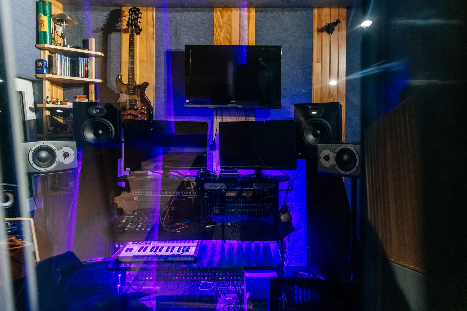 La cabine du studio vue à travers la vitre : écoutes, écrans et clavier dans une lumière violette